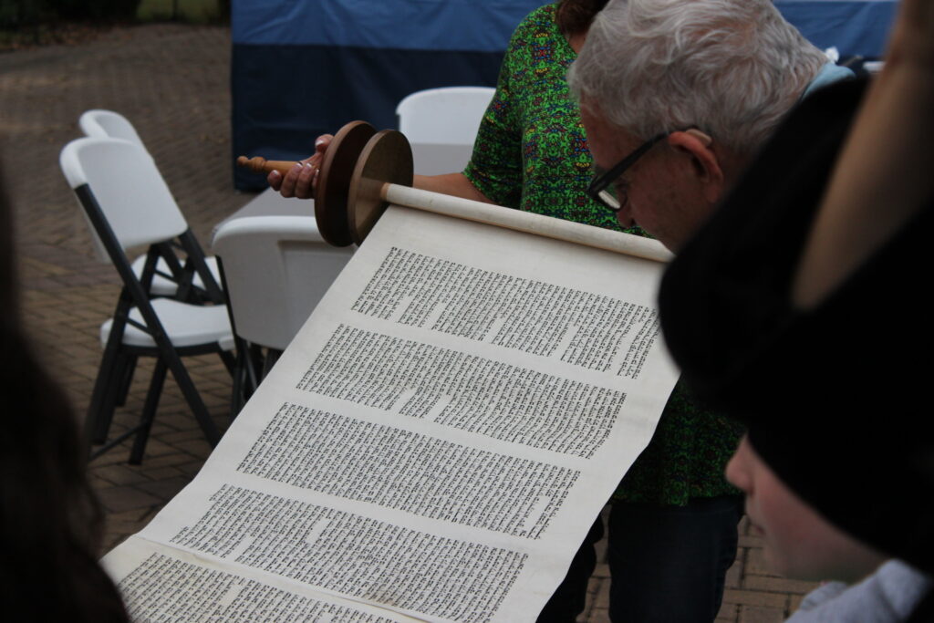Person reading an ancient scroll with Hebrew text outdoors.