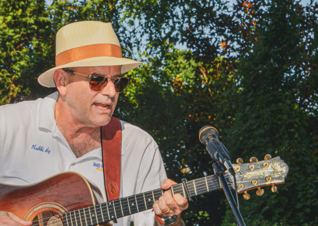 Man playing guitar outdoors, wearing a hat and sunglasses.