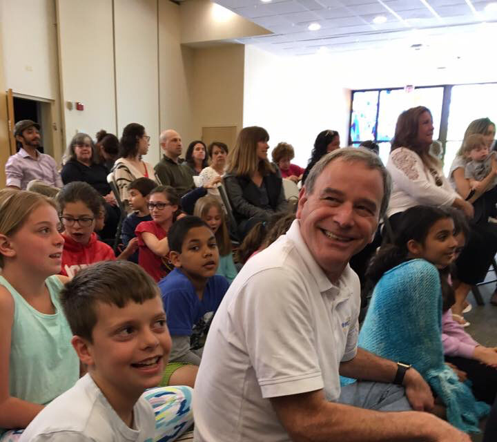 A group of children and adults sitting and smiling indoors.