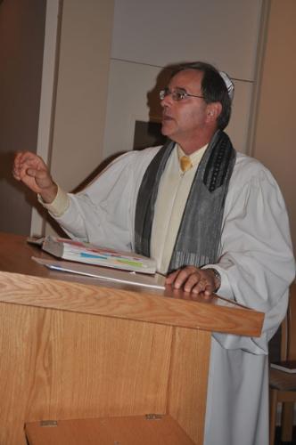 Man speaking at a podium wearing a white robe and scarf.