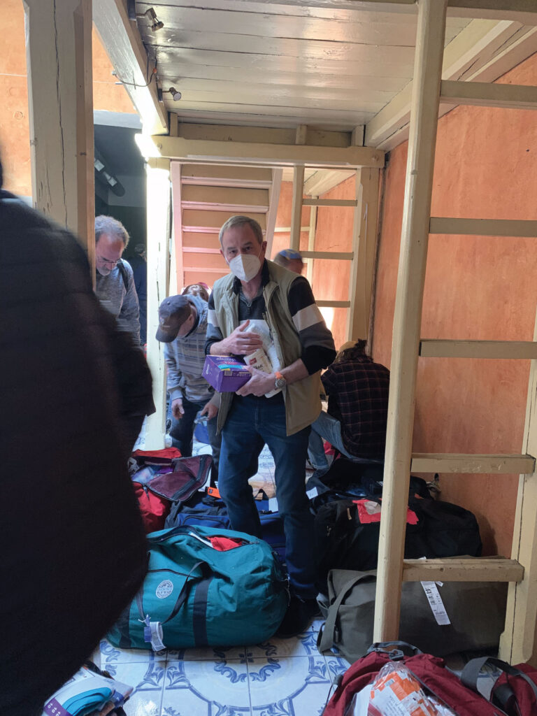 People with luggage inside a narrow indoor space, some wearing masks.