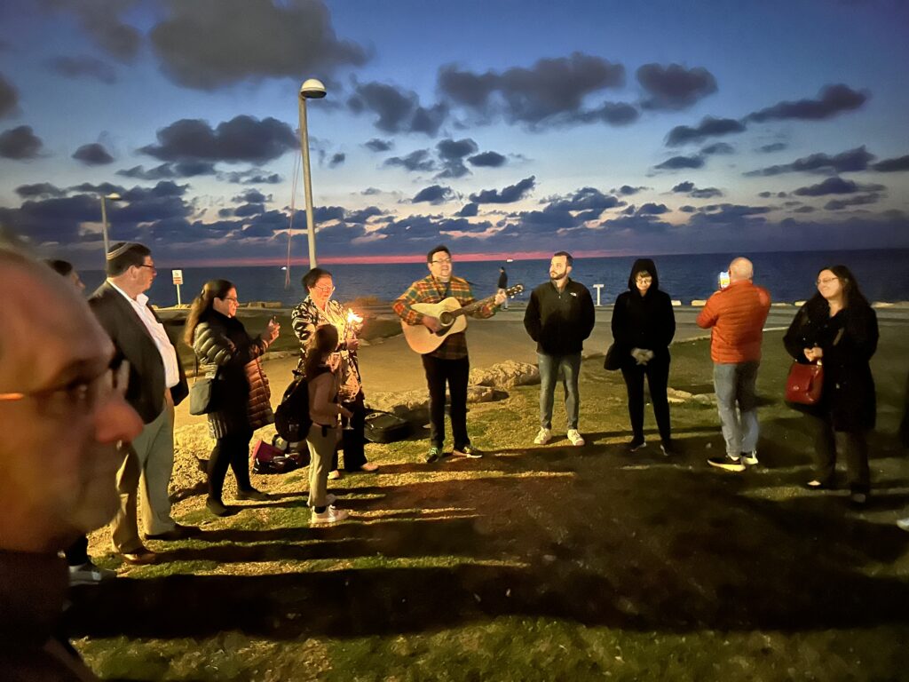 Group gathered outdoors at dusk with guitar player.