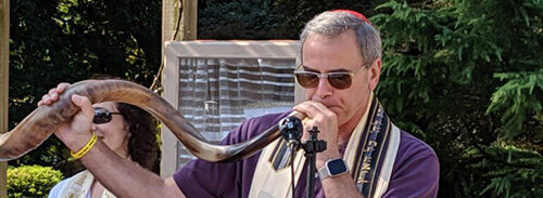 Man reading from a book with a prayer shawl outdoors.