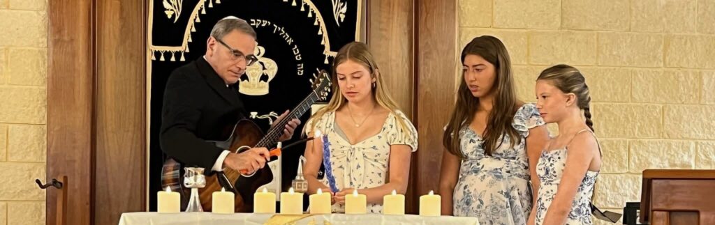 A man performs a ceremony with three girls at a table with candles.