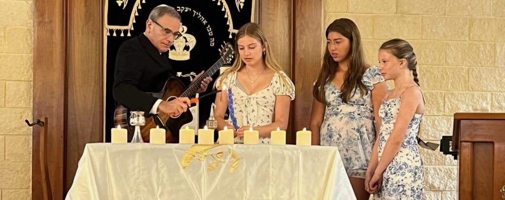 A man in religious attire leads a ceremony with three girls at a table with candles.