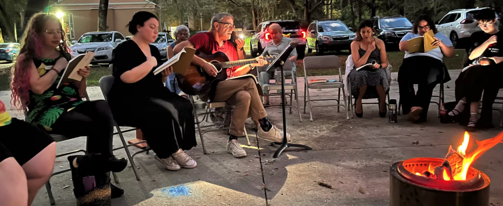 People enjoying an outdoor music session around a fire pit.