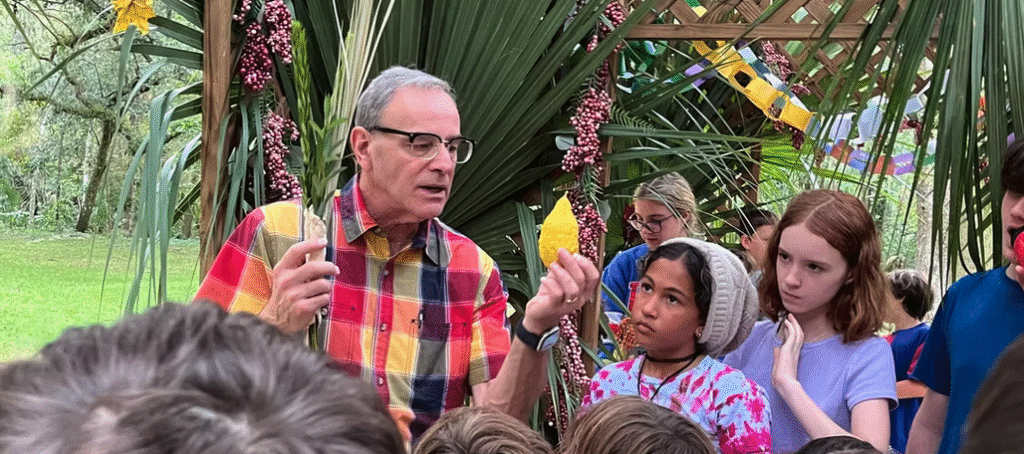 An older man enthusiastically teaches a group of children outdoors.