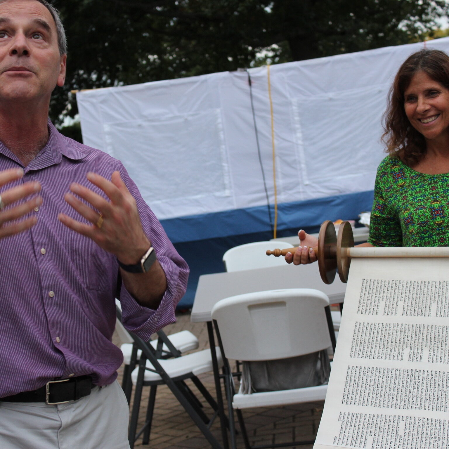 A man and woman speaking outdoors near a table with a large printed document.