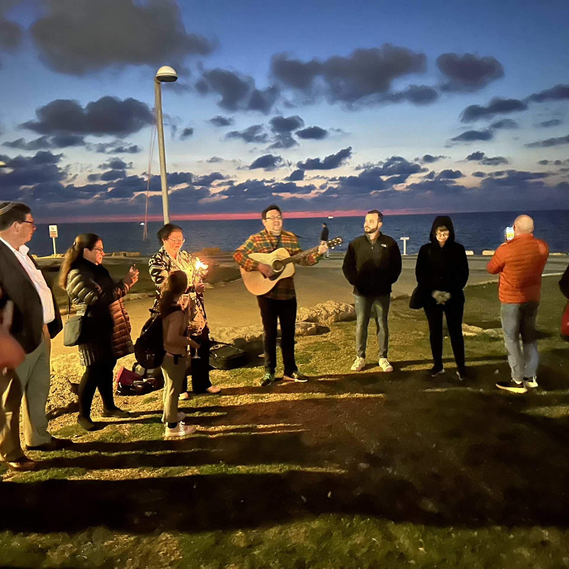 Group gathered outdoors at dusk with guitar player.