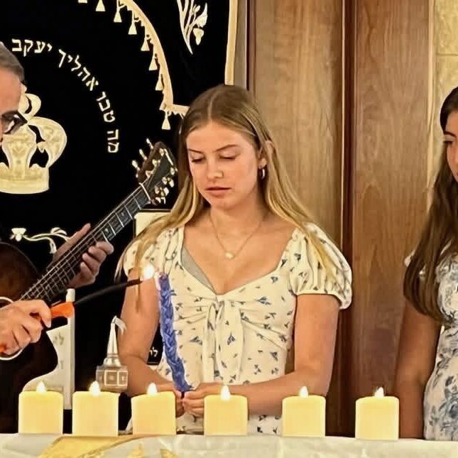 A man performs a ceremony with three girls at a table with candles.