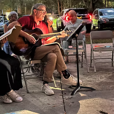 Group of musicians playing outdoors around a campfire.