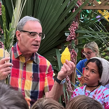 An older man enthusiastically teaches a group of children outdoors.