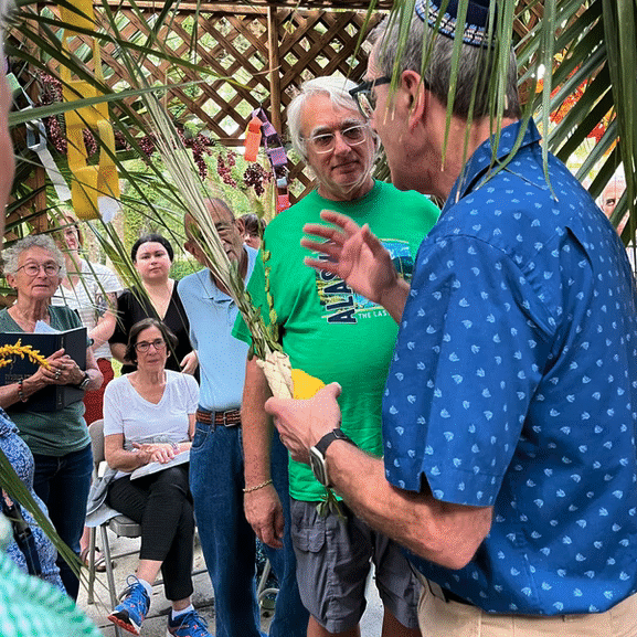 Two men engaging in a conversation during an outdoor event with people around.