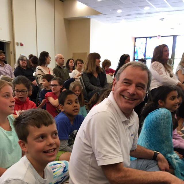 A group of children and adults sitting and smiling indoors.