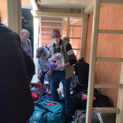 People packing bags in a narrow room, preparing for travel or relocation.