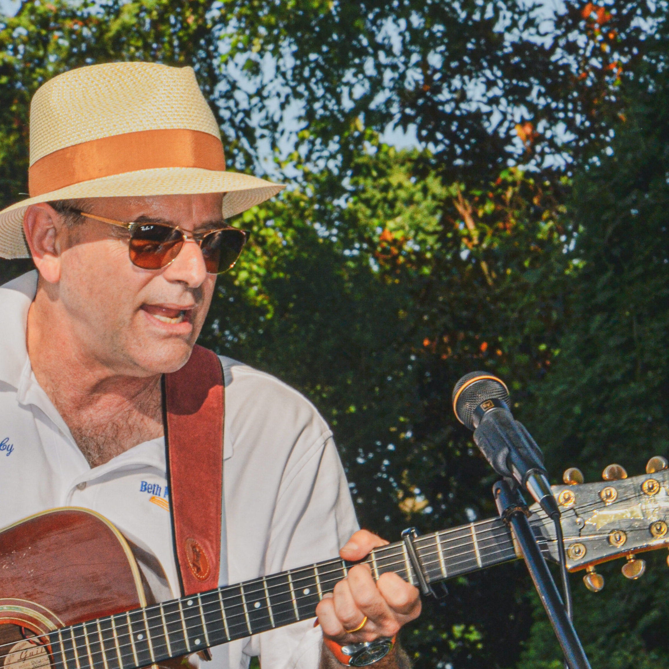 Man playing guitar outdoors, wearing a hat and sunglasses.