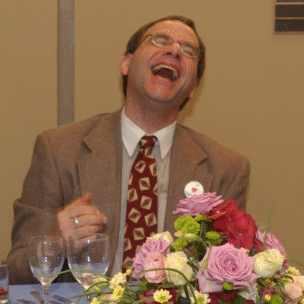 Man laughing joyfully at a formal event with flowers.