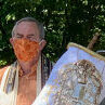 A man wearing an orange mask holds a decorated scroll outdoors.