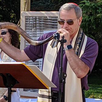 Man reading from a book with a prayer shawl outdoors.