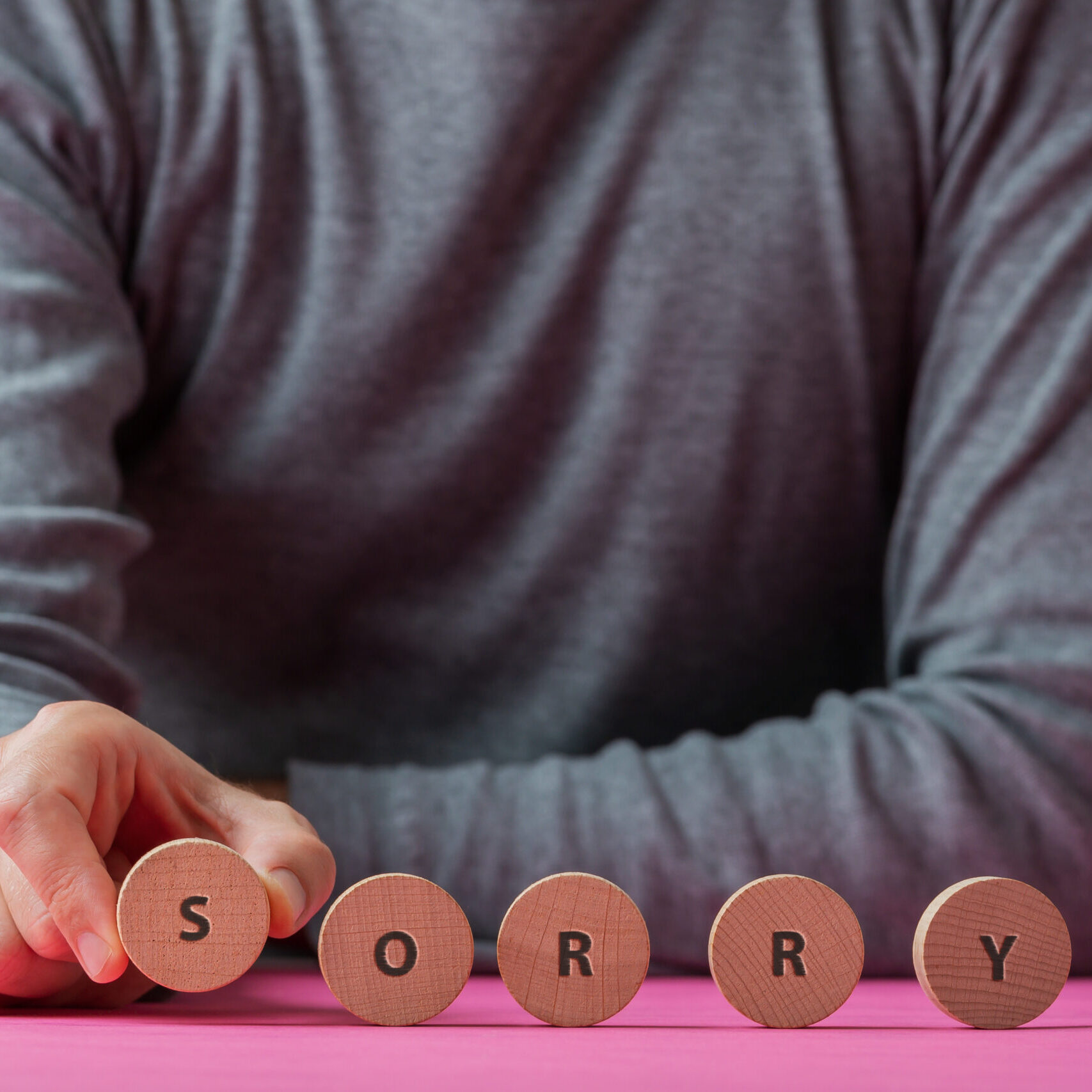 Sorry sign on wooden cut circles Front view of a man making a Sorry sign spelled on wooden cut circles.