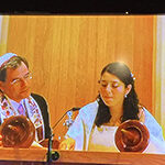 Two women in traditional attire engaged in a cultural event with wooden objects.